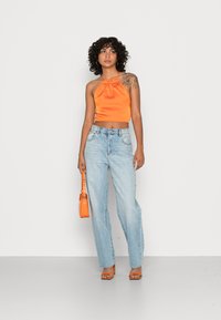 Top halter laranja de cetim com decote franzido, combinado com jeans de cintura alta azul claro. Os acessórios incluem uma pequena mala laranja.