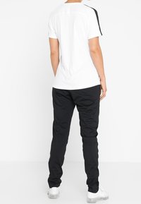 Sportoutfit som består av en vit kortärmad tröja med svarta detaljer och svarta byxor. Materialet verkar vara lätt och ha en slät yta.