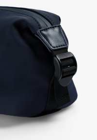 Neceser de color azul marino con una superficie de tela suave, que presenta un acento de cuero texturizado y un cierre de hebilla ajustable para un cierre seguro.