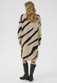 Gebreid jurkje in beige met zwarte zebra-strepen, lange mouwen en een relaxte pasvorm, gecombineerd met kniehoge zwarte laarzen met gespen.