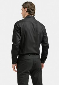 Svart skjortklänning med en jämn yta, standardkrage, knäppta manschetter och figurnära design, i kombination med mörka skräddarsydda byxor.