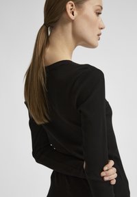 Fekete bordázott, hosszú ujjú felső kerek nyakkivágással. Feszes szabású és sima tapintású. A modellen hosszú haja van, amit lófarokba kötött.