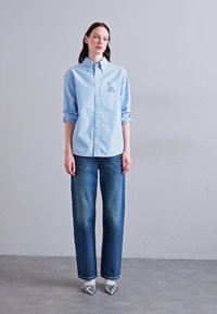 Cămașă albastră deschis cu mâneci lungi, asociată cu blugi negri drepti, stilizată cu pantofi gri cu model.