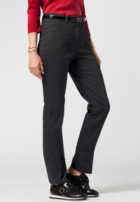 Pantaloni in denim nero con taglio dritto, dotati di tasche anteriori e una cintura nera lucida. Indossati con eleganti sneakers nere e una maglietta rossa.