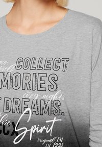 Graues Langarmshirt mit schwarzem und weißem Text sowie Strassakzenten, der "Sammle Erinnerungen" sagt, und einem verblassten Designverlauf.