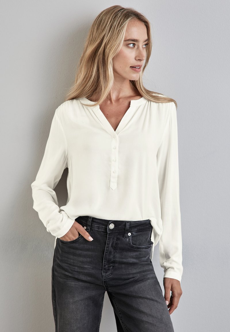 Chemise blanche à manches longues avec un col en V et cinq boutons, associée à un jean en denim foncé taille haute. Texture lisse, coupe décontractée.