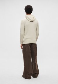 Hoodie de malha bege claro com cordão, textura canelada e mangas compridas, combinado com calças de perna larga castanho-escuras. Vista de trás.