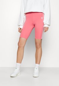 Růžové cyklistické šortky s elastickým pasem, s třemi bílými pruhy po stranách a logem Adidas na levé noze.