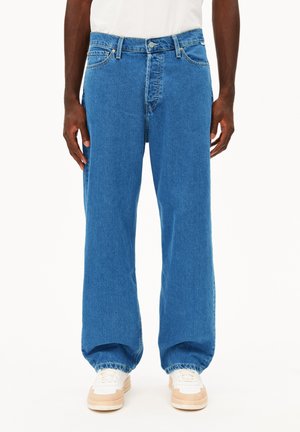 Wijdvallende blauwe denim jeans met een licht vervaagde structuur, hoge taille, riemlussen en klassiek vijf-pocketdesign, gecombineerd met witte sneakers.