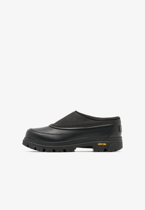 Schwarzer Slip-On-Clog mit dicker, profillierter Sohle und Vibram-Logo an der Ferse, entwickelt für den Außenbereich und den Freizeitgebrauch.