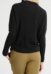 Black ribbed sweater with a high neckline and long sleeves, paired with beige trousers, featuring a relaxed fit and textured fabric.