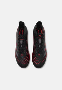 Botas de fútbol negras con acentos rojos y superficie texturizada. Cuentan con un diseño de cordones, forma aerodinámica y suela curva para mayor agilidad.