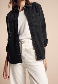 Svart, knäppt denimskjorta med två framsidans fickor, bärs över en vit skjorta, tillsammans med vita högmidjade byxor. Slät textur, avslappnad passform.