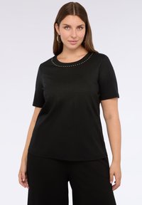 Camiseta negra de manga corta con cuello redondo, con un diseño texturizado y pequeños remaches plateados alrededor del cuello.