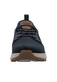 Baskets bleu marine avec une tige texturée, des accents bruns contrastants et des lacets à pois blancs. Semelle flexible avec une base beige clair.