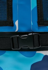 Blå camouflage-mønstret materiale med en glat tekstur, sort justerbar spænde og mesh-detaljer.