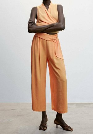 Oranžový komplet s překládaným topem a kalhotami se širokými nohavicemi z texturované látky. Výrazné detaily zahrnují zavazování v pase s kulatým ozdobným prvkem a boční kapsy.