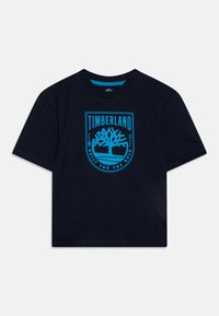 T-shirt en coton bleu marine avec col rond, arborant un logo et un graphique d'arbre Timberland turquoise au centre. Manches courtes ; coupe décontractée.