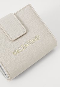 Beige skinnveske med teksturert overflate, med klaffelukking og gull "VALENTINO"-logo foran. Kompakt design med runde kanter.