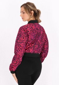 Jachetă bomber cropped roz și neagră cu un model în dungi de zebra, având un guler și manșete ribelate negre. Fabricată dintr-un material ușor.