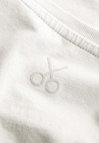 Witte katoen met een subtiele, geborduurde scharenmotief in een lichtgrijze tint vlakbij de halslijn. Gladde textuur, minimalistisch ontwerp.