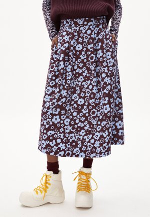 Bloemrijke midi-rok met een bruine basis en lichtblauwe patronen, gemaakt van stof met een lichte glans, gecombineerd met helderwitte laarzen.
