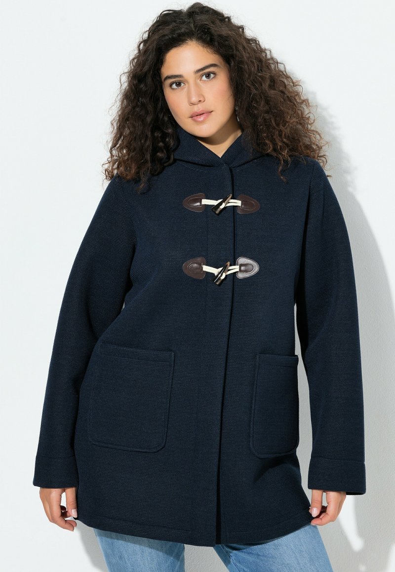 Tmavě modrý vlněný kabát s kapucí, vybavený zapínáním na kloubové uzávěry a dvěma náprsními kapsami, navržený v uvolněném střihu s texturovaným povrchem.