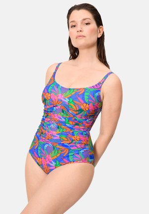 Mujer con cabello largo y oscuro que lleva un traje de baño de una pieza vibrante con patrones florales tropicales en azul, verde, naranja y rosa, posando contra un fondo blanco.