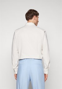 Camicia beige chiaro con un motivo testurizzato, polsini con bottoni e colletto classico abbinata a pantaloni su misura blu chiaro.