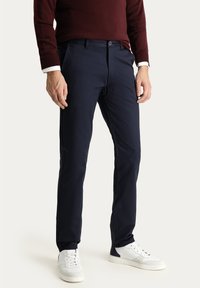 Marineblau Hosen aus leichtem Stoff, mit schlankem Schnitt, Seitentaschen und Reißverschluss, kombiniert mit weißen Sneakers.