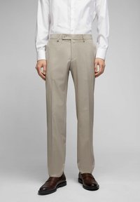 Beige maßgeschneiderte Hose mit feiner Textur und einem einzelnen Bundfalten. verfügt über einen Klettverschluss und Seitentaschen. Kombiniert mit dunkelbraunen Schuhen.