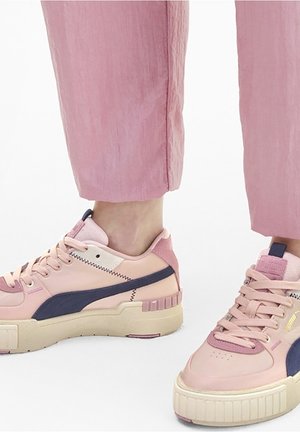 Vaaleanpunaiset sneakersit, joissa on yhdistettyjä sileitä ja teksturoituja materiaaleja, laivastonsiniset yksityiskohdat ja paksu pohjakuvio. Nyöritettävä sulkemismekanismi.