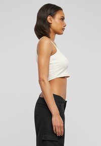 Débardeur crème court avec bretelles fines, associé à un pantalon cargo noir taille haute. Texture lisse et design simple.
