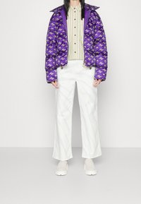 Paarse donzen jas met een patroon, gecombineerd met een gestreept overhemd en witte broek met wijde pijpen; compleet met witte instapschoenen.