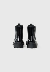 Botas de tobillo de charol negro con suela gruesa, paneles laterales elásticos y lengüetas en la parte trasera para facilitar su uso.