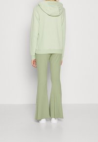 Ljusgrön hoodie med huva, kombinerad med ribbade, utsvängda gröna byxor. Vita skor fulländar outfiten. Slätt material, avslappnad passform.