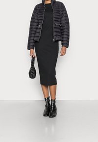 Svart puffjacka med horisontell sömnad, fickor med dragkedja, bärs över en figurnära svart ribbad midiklänning. Svarta ankelskor och en flätad handväska.