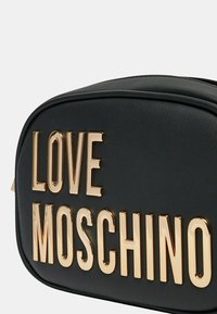 Borsa sintetica nera con lettering "LOVE MOSCHINO" in tonalità dorata. Forma arrotondata, texture liscia e cuciture visibili lungo le cuciture.
