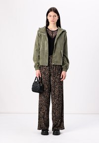 Kaki kordura jakna s kapuljačom, crni čipkani top, široke hlače s leopard uzorkom, crna teksturirana torba, masivne crne cipele.