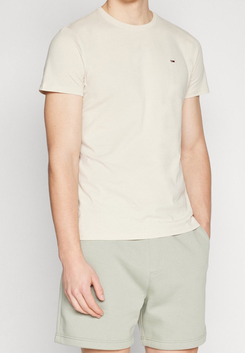 Beige bavlněné tričko s krátkými rukávy, kulatým výstřihem a malým vyšitým logem. Spárované se světle zelenými šortkami.