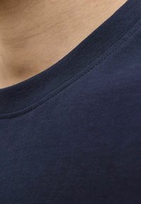 Tumši zils apģērba T-krekls ar gludu tekstūru un ribotu apkakli. Iespējo vienkāršu, tīru dizainu, kas piemērots ikdienas valkāšanai.