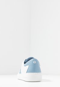 Biały i jasnoniebieski sneaker z teksturowaną cholewką, gładkimi skórzanymi akcentami oraz białą podeszwą z logo z tyłu.