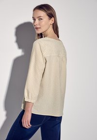 Blusa a quadri beige chiaro con maniche a tre quarti, scollo tondo e orlo dritto. Realizzata in tessuto testurizzato con un motivo sottile.