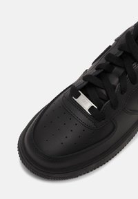 Baskets en cuir noir vue de face avec des lacets noirs et une petite plaque métallique gravée "AF1" sur le panneau des lacets.