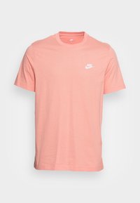 Triko s krátkým rukávem a kulatým výstřihem v jemně růžové barvě z bavlny, s malým bílým logem Nike na levé straně hrudi. Hladký materiál, standardní střih.