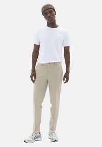 Pantalon beige ajusté associé à un t-shirt blanc à col ras du cou et des baskets grises. La tenue comprend un bonnet tricoté brun.