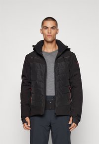 Schwarze isolierte Jacke mit Kapuze, ausgestattet mit gesteppter Polsterung auf der Vorderseite, Reißverschlusstaschen und einem grauen Pullover darunter.