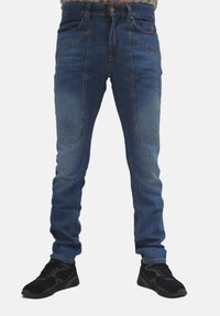 Jeans in denim blu con una vestibilità slim, dotati di due tasche anteriori e un effetto di lavaggio sbiadito. Abbinati a scarpe sportive nere.