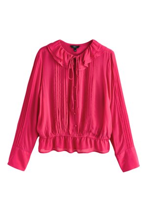 Blouse rose vif à manches longues avec col et ourlet à volants, plis verticaux sur le devant et les manches, boutons recouverts de tissu, et lien noué à l'avant du cou.