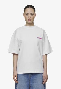 Hvit oversized bomull T-skjorte med korte ermer, rund halsutringning, og en liten rosa logo på venstre bryst.